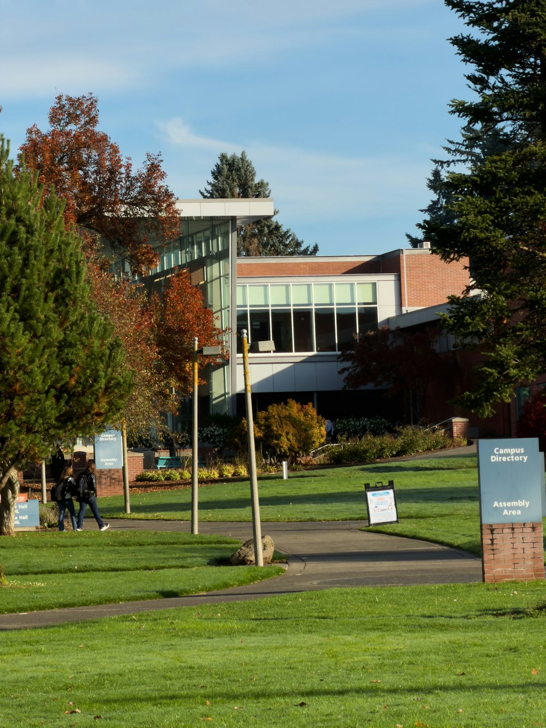 Students walk on a campus path surrounded by autumn trees and buildings.