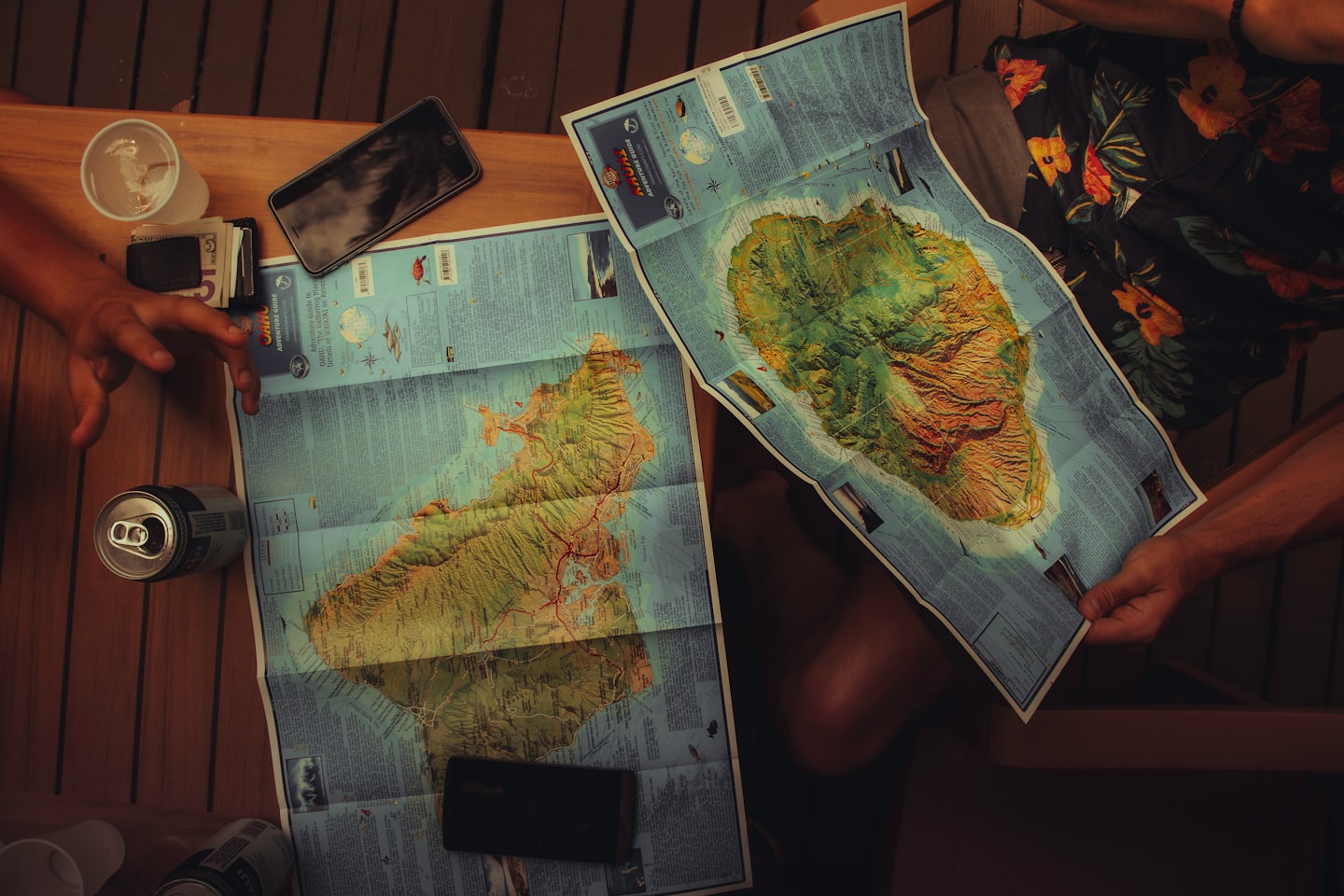 Two people examine topographical maps on a wooden table.