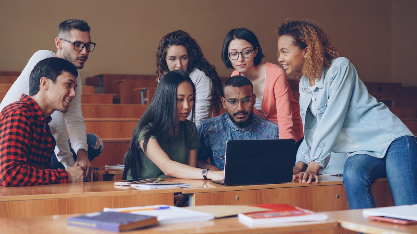 University students collaborating around a laptop in a lecture hall.